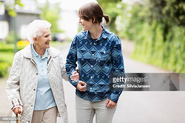 young woman helping elderly woman walk down street - senior woman walking stock pictures, royalty-free photos & images
