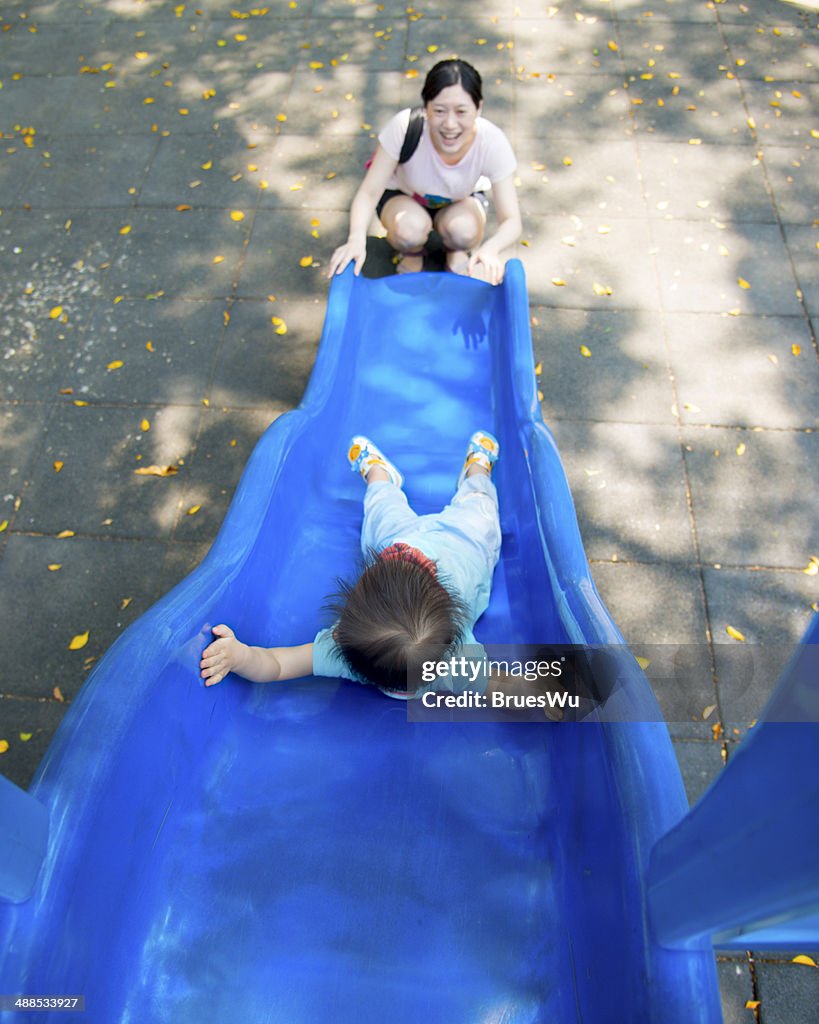 Baby playing on the slide with young Mom