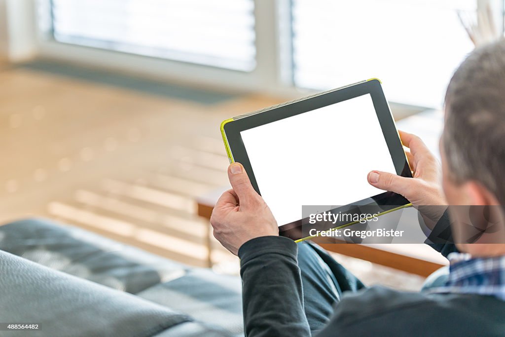 Idoso sentado no sofá usando tablet digital
