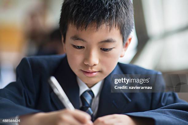 giapponese studente ragazzo che lavora alla sua scrivania in aula - uniforme scolastica foto e immagini stock