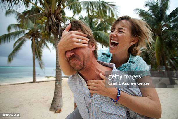 woman covering mans eyes while riding on back. - bartstoppel stock-fotos und bilder