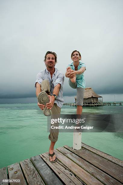 man and woman attempting yoga pose on dock post. - bartstoppel stock-fotos und bilder