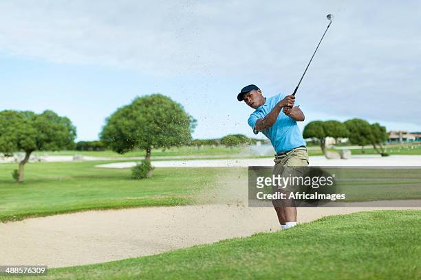 african golfer getting his ball out of the bunker. - young men golfing stock pictures, royalty-free photos & images