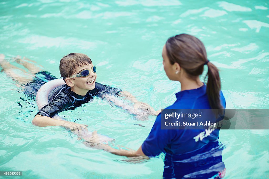 Young boy learning to swim in pool with teacher