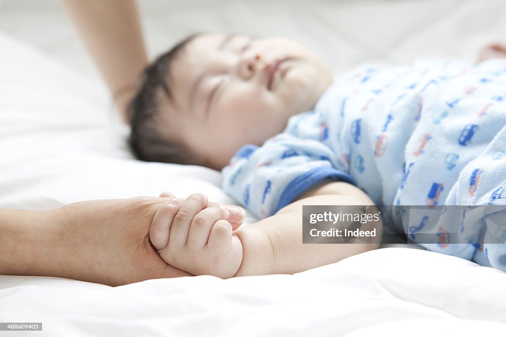 Mother holding baby's hand in bed