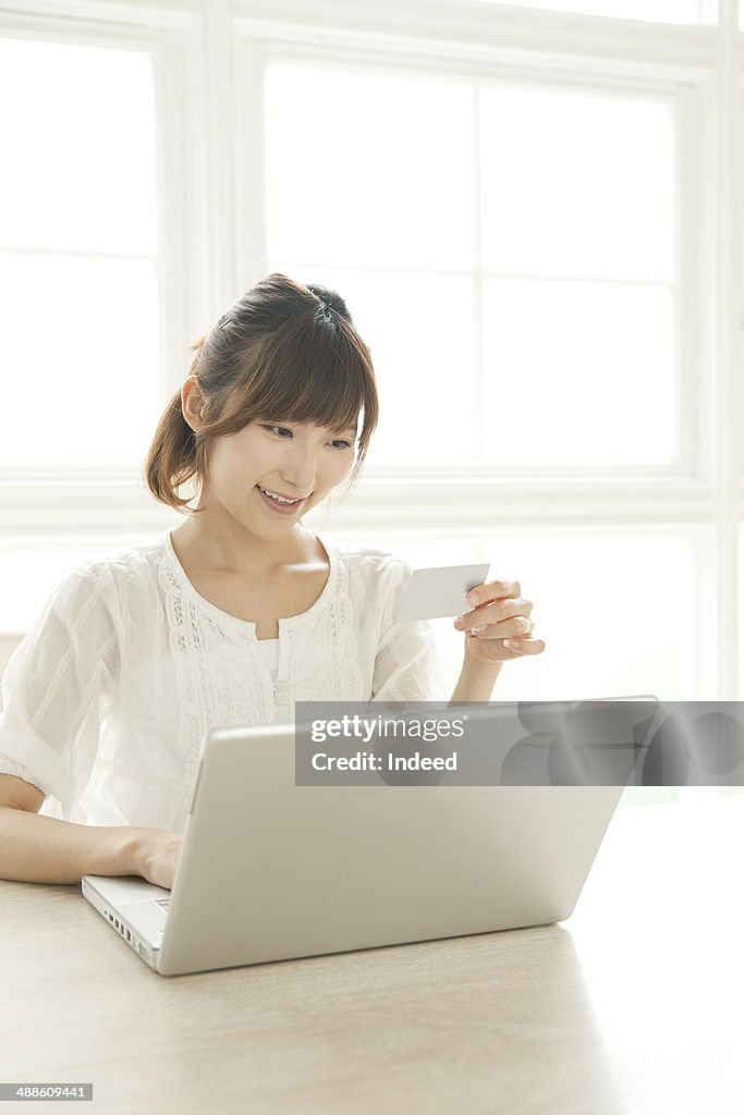 Young woman using laptop in room, holding a credit card