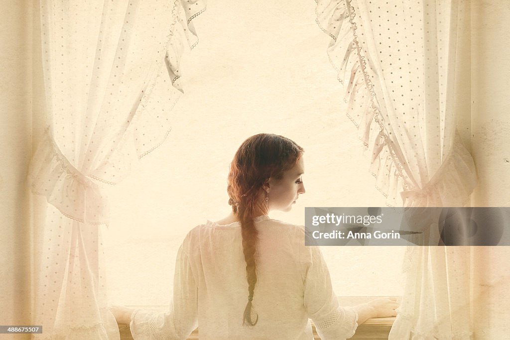 Woman with braid at window framed by curtains