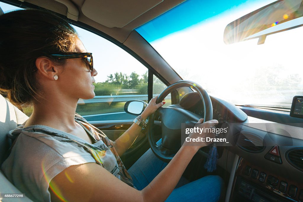 Young woman driving car and speeding on highway in summer