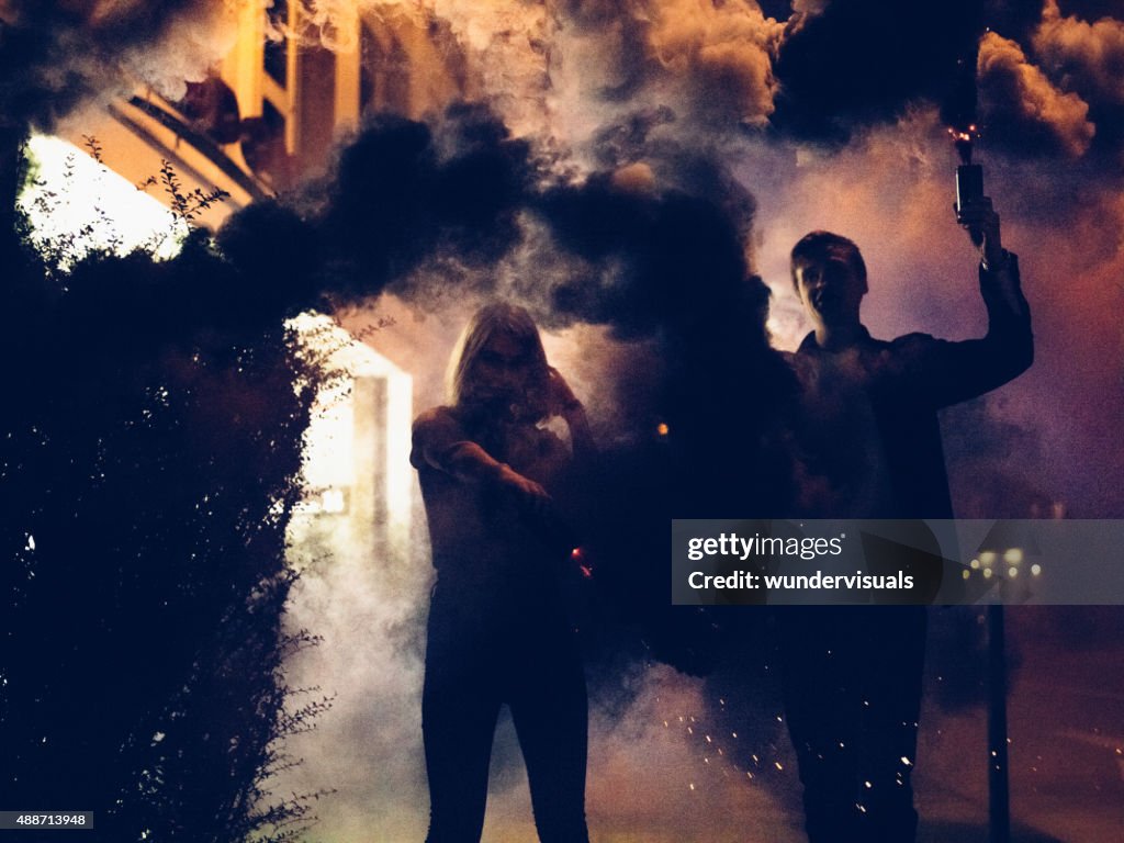 Young couple holding smoke flares at night in the city