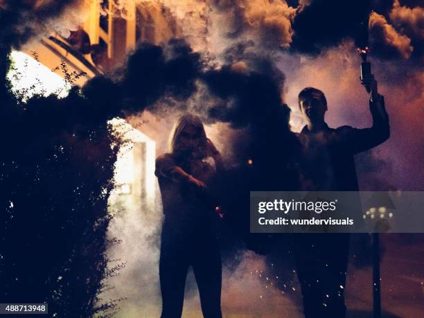 young couple holding smoke flares at night in the city - distress flare stock pictures, royalty-free photos & images