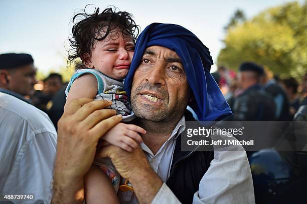 Man holds his crying child close to him as migrants force their way through police lines at Tovarnik station for a train to take them to Zagreb on...
