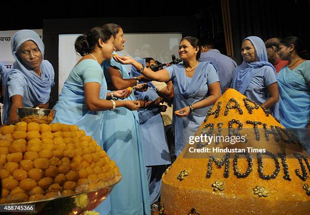 The lady workers of Sulabh International partake from a huge 365-kg weighing Laddoo during the celebrations of Prime Minister Narendra Modi's...