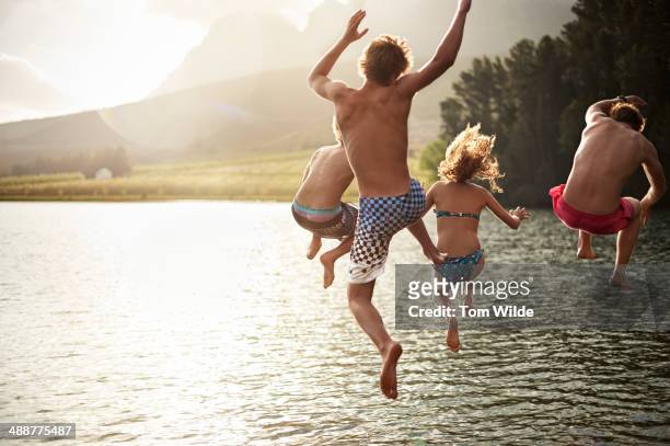 four friends jumping into a lake in the mountains - lago foto e immagini stock