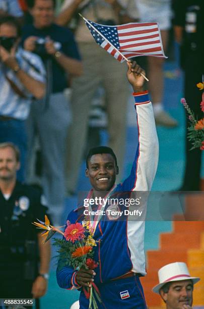 American athlete Carl Lewis waves the Stars and Stripes after being awarded a gold medal at the Los Angeles Memorial Coliseum during the Olympic...