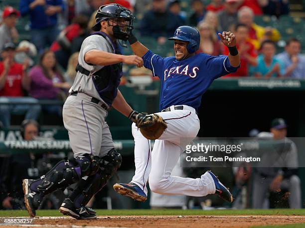 Alex Rios of the Texas Rangers slides into home plate against catcher Michael McKenry of the Colorado Rockies to score in the bottom of the second...