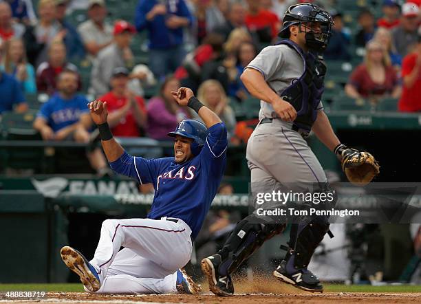 Alex Rios of the Texas Rangers slides into home plate against catcher Michael McKenry of the Colorado Rockies to score in the bottom of the second...