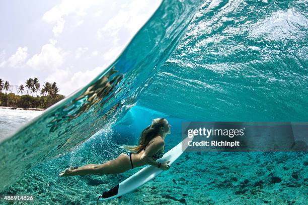 over/under of surfer girl duck diving tropical waves - surf girl stock pictures, royalty-free photos & images