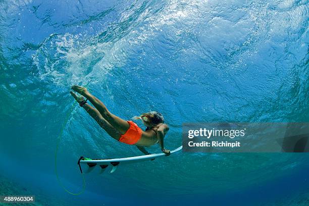 surfer girl in orange shorts duck dives a wave - board shorts stock pictures, royalty-free photos & images