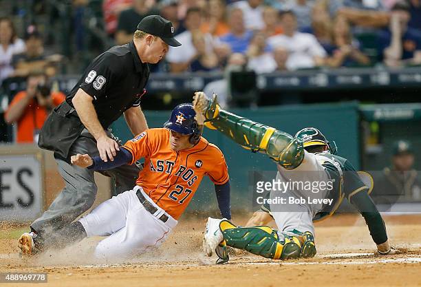 Jose Altuve of the Houston Astros scores as he slides past Carson Blair of the Oakland Athletics as home plate umpire Toby Basner makes the call in...