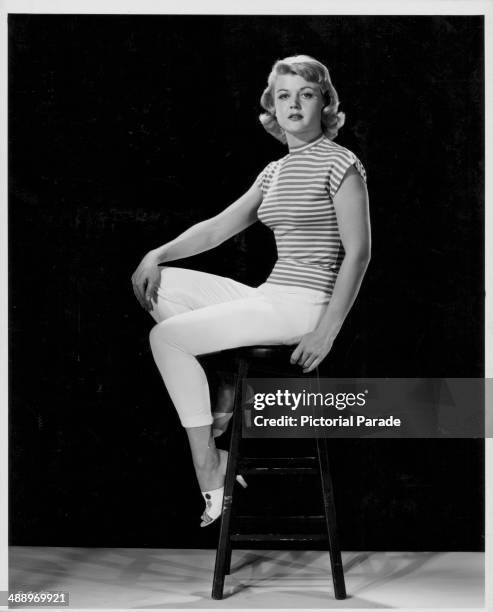 Promotional portrait of actress Angela Lansbury, wearing white trousers and a striped blouse, 1955.