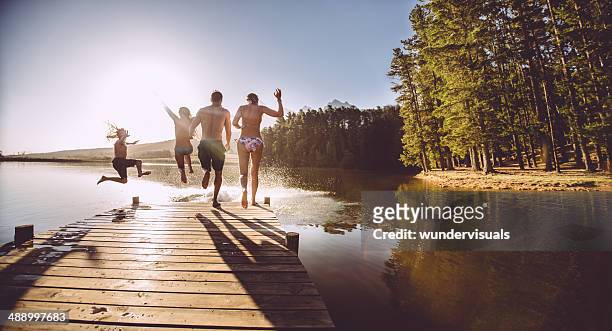 four people jumping off a jetty into the water - swimming stock pictures, royalty-free photos & images