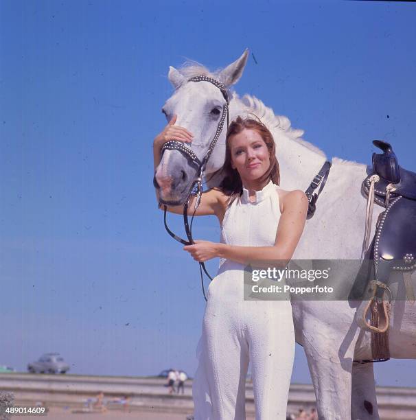 English actress Diana Rigg stands with a white horse in her role as 'Emma Peel' in the television series 'The Avengers', Camber Sands, East Sussex,...