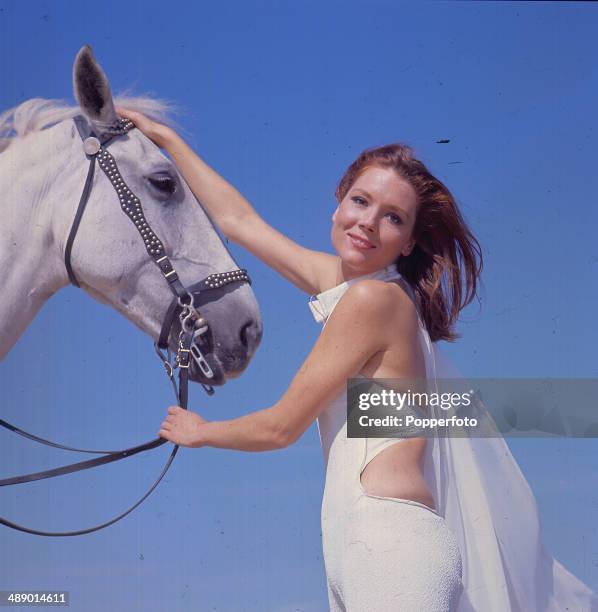English actress Diana Rigg stands with a white horse in her role as 'Emma Peel' in the television series 'The Avengers', Camber Sands, East Sussex,...