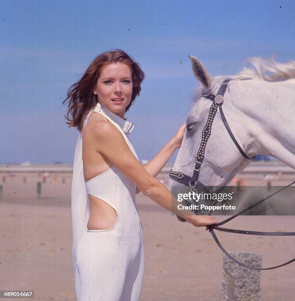 English actress Diana Rigg stands with a white horse in her role as 'Emma Peel' in the television series 'The Avengers', Camber Sands, East Sussex,...