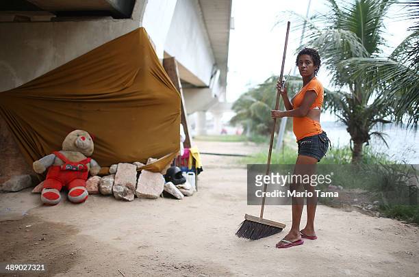 Viviane Sabino de Souza poses while sweeping in front of her makeshift dwelling beneath a stretch of the Transcarioca BRT highway being constructed...