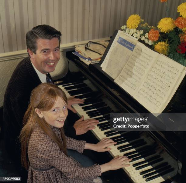 English comedian and host Leslie Crowther posed at the piano at home with his daughter, actress Liz Crowther in 1967.