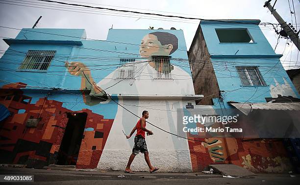 Man walks past community artwork painted by Dutch artists Jeroen Koolhaas and Dre Urhahn in the Vila Cruzeiro shanty town on May 9, 2014 in Rio de...