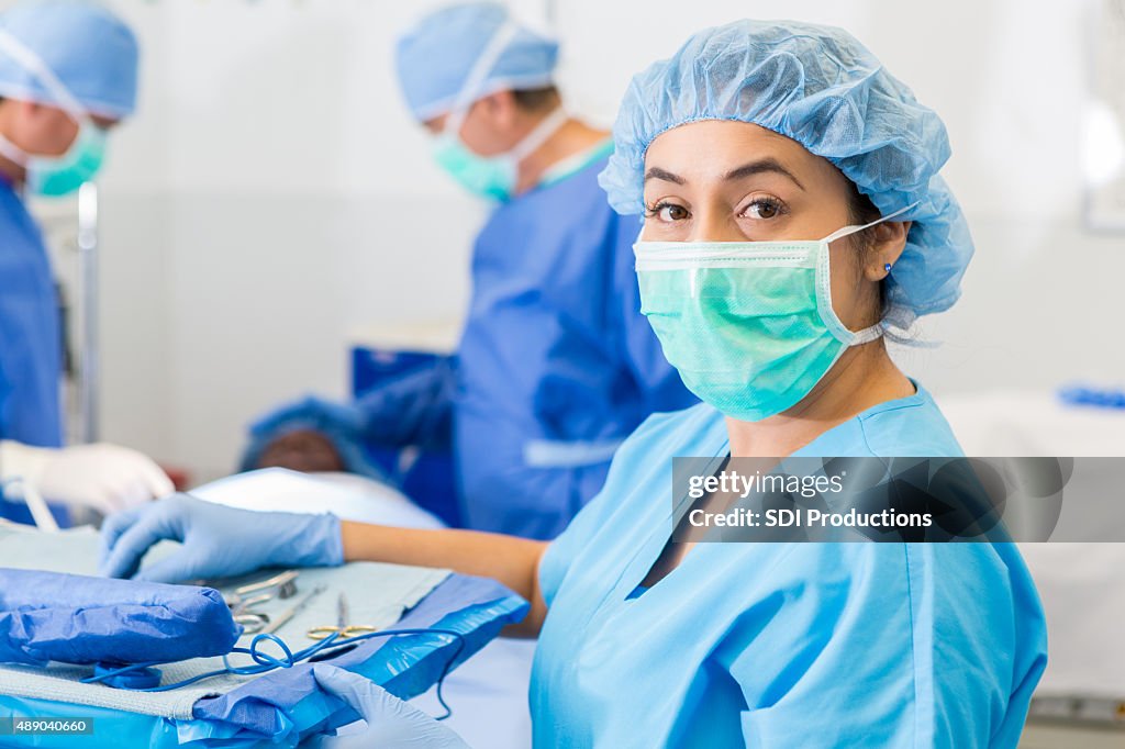 Hispanic surgical nurse or technician assisting with surgery in hospital