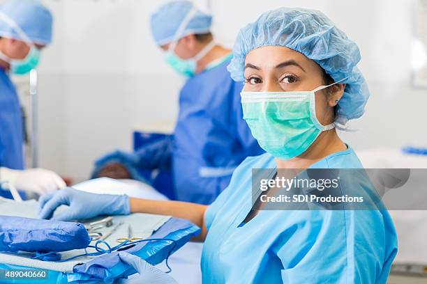 hispanic surgical nurse or technician assisting with surgery in hospital - surgical equipment stockfoto's en -beelden