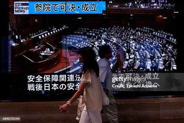 People walk past a big screen showing news about the House of Councillors ratifying Japan's security bill on September 19, 2015 in Tokyo, Japan....