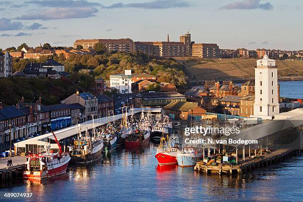 Fishing boats and lighthouse in North Shields on the Tyne river, with the town of Tynemouth in the background.