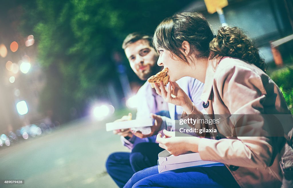 People eating pizza in the street.