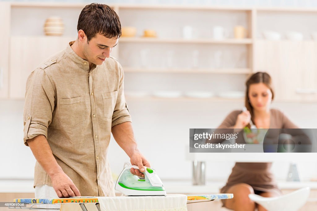 Smiling young man ironing clothes at home.