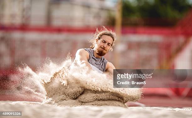 athletic man landing in a sand after a long jump. - long jumper stock pictures, royalty-free photos & images