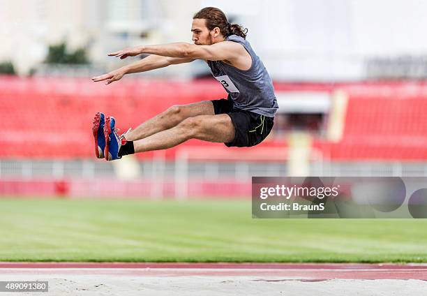 young male athlete in a long jump on a stadium. - verspringen stockfoto's en -beelden