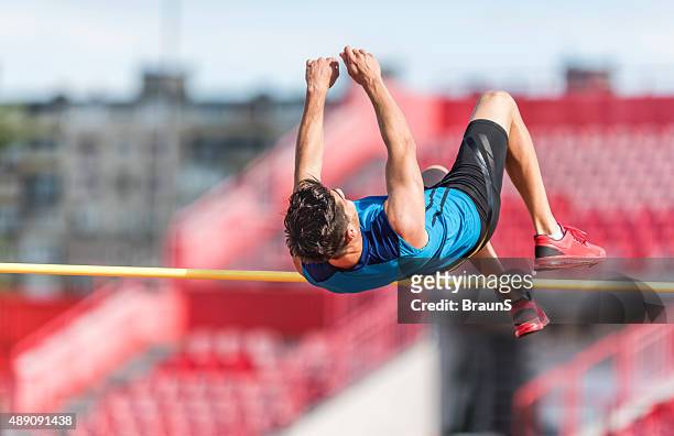 sportlichen mann performing high jump auf einem wettbewerb. - hochsprung stock-fotos und bilder