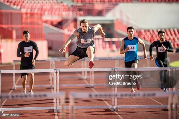 young male athletes jumping hurdles on a sports race. - hordelopen atletiekonderdeel stockfoto's en -beelden