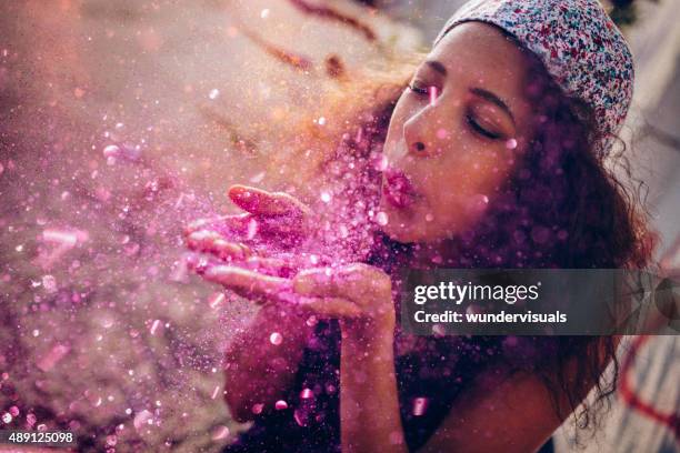 Afro American teen girl blowing pink sparkling glitter outdoors