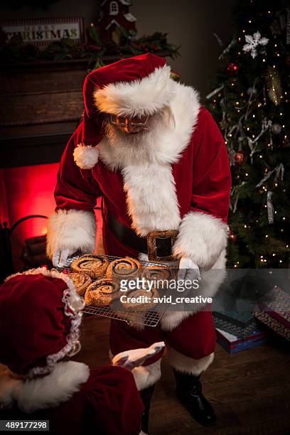 santa giving ms. claus cinnamon rolls - mrs claus stock pictures, royalty-free photos & images