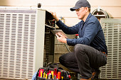 Air conditioner repairman works on home unit. Blue collar worker.