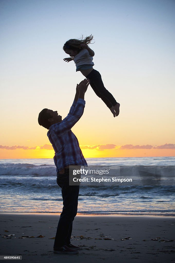 Father tossing his daughter at the beach, sunset