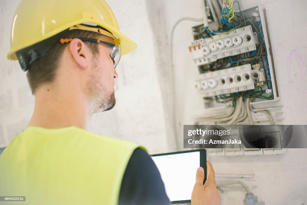 Electrician reviewing plans on digital tablet at construction site