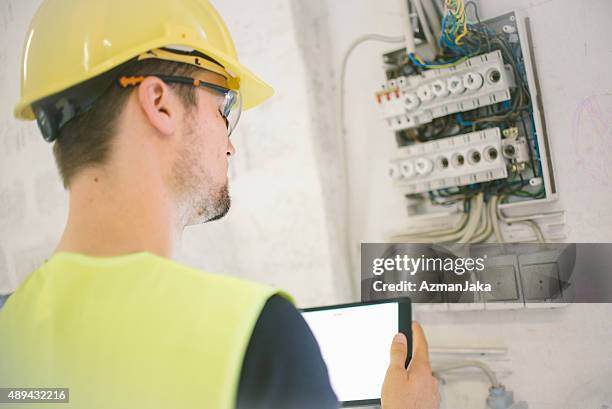 electrician reviewing plans on digital tablet at construction site - distribution board stock pictures, royalty-free photos & images