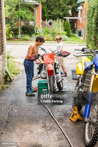 two brothers cleaning their dirt bikes in the driveway. - motorcross stock pictures, royalty-free photos & images