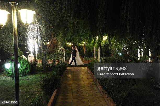 An Iranian couple walks along a pathway lined by fireworks at a luxury wedding with mixed dancing and removal of headscarves, at a private garden...