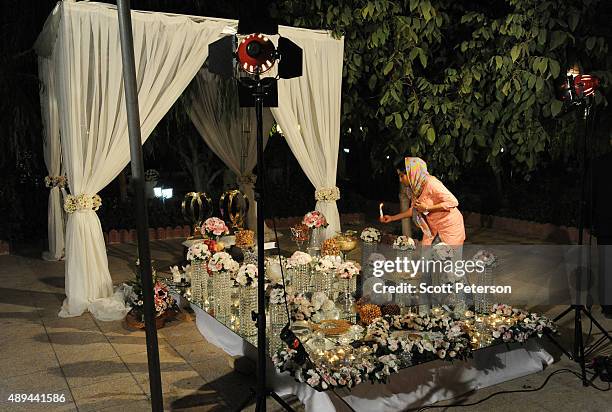An Iranian woman lights candles on an elaborate table laid out with flowers and glass ornaments for a luxury wedding with mixed dancing and removal...